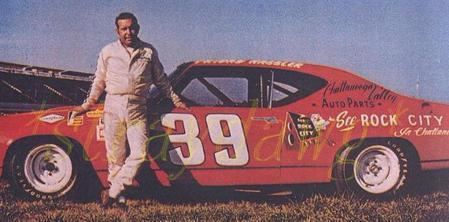 Friday Hassler is smiling and standing beside his red racing car, wearing a white jacket, white pants, and black shoes.