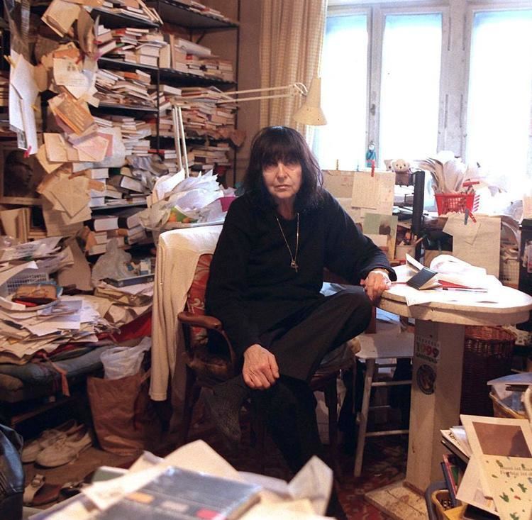 Friederike Mayröcker inside a messy room wearing all-black clothes