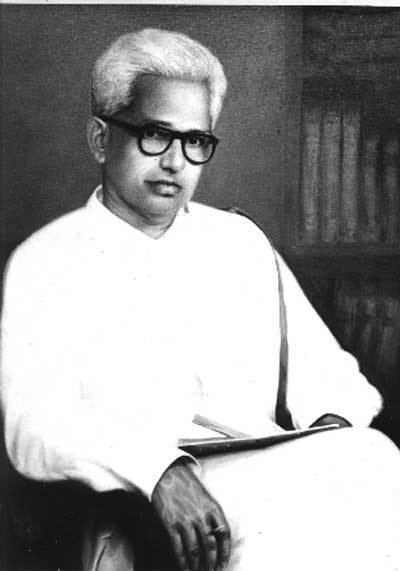 G. Sankara Kurup with a serious face and wearing eyeglasses and white long sleeves with a book on his lap.