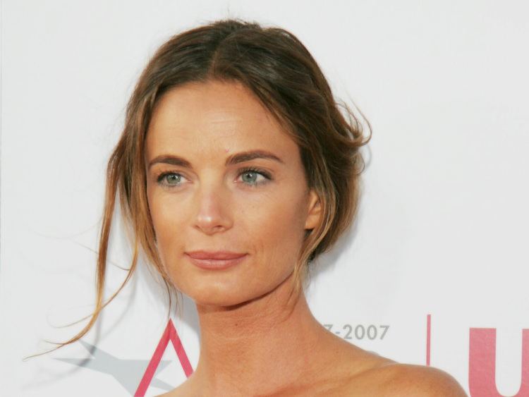 Gabrielle Anwar with an "American film institute" wallpaper on the background, she is smiling with her blonde hair