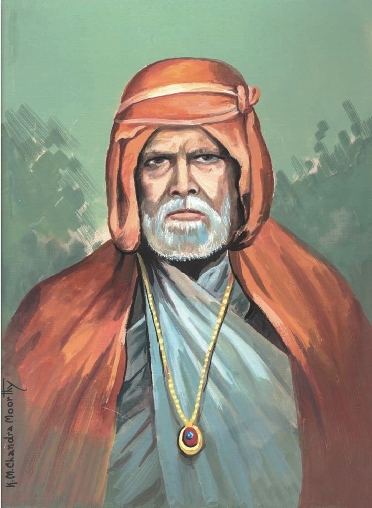 Gadge Maharaj with a serious face and a grey beard while wearing a long gold necklace and a turban, traditional Indian clothing