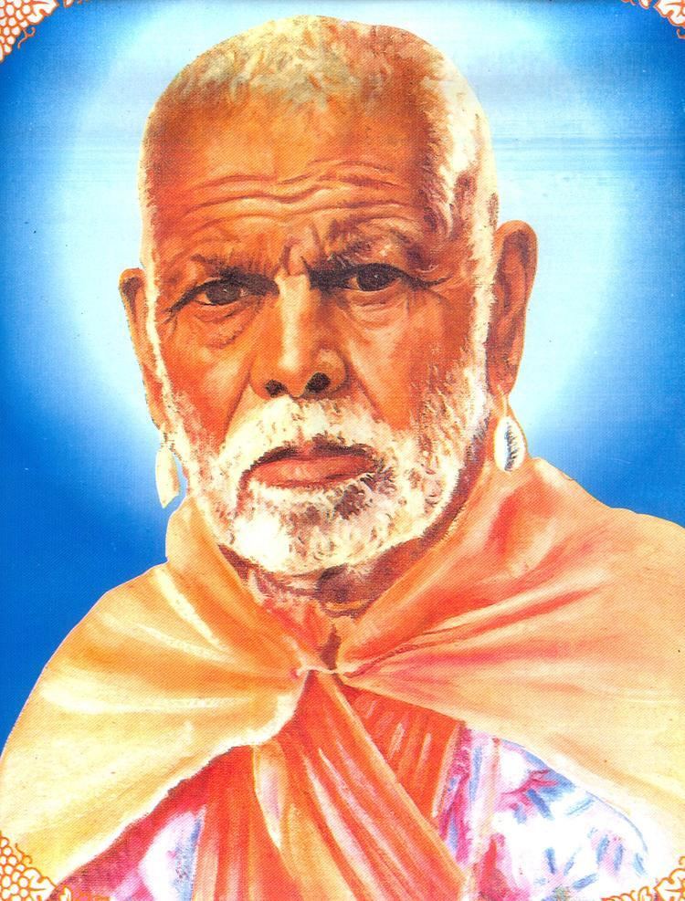 Gadge Maharaj with a serious face and with a grey beard wearing earrings and traditional Indian clothing.