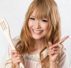 Gal Sone smiling while holding a spatula and wearing a cream blouse