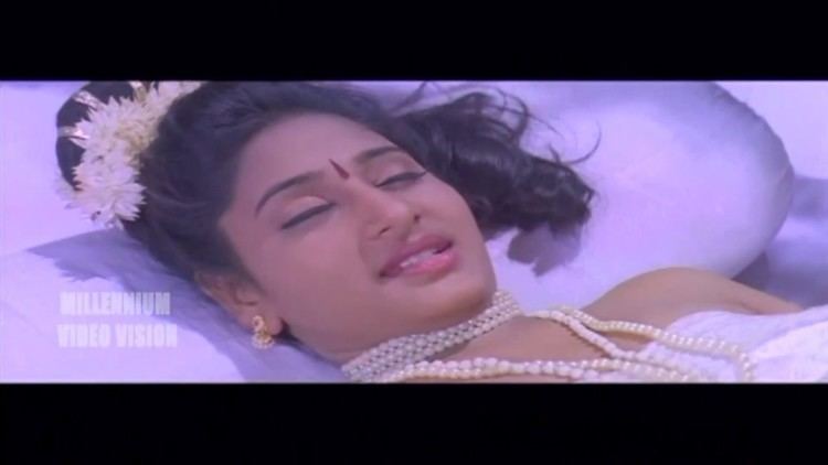 A woman smiling while lying on the bed and wearing a pearl necklace in a scene from the 2000 Indian Malayalam film, Gandharva Rathri