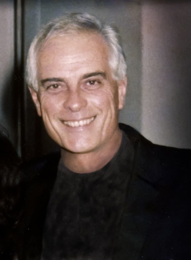Gardner McKay smiling while wearing a black coat and black shirt