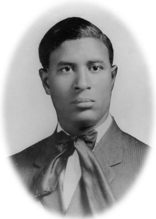 Garrett Augustus Morgan, Sr. with a serious face, wearing a coat over white long sleeves and a ribbon bowtie.