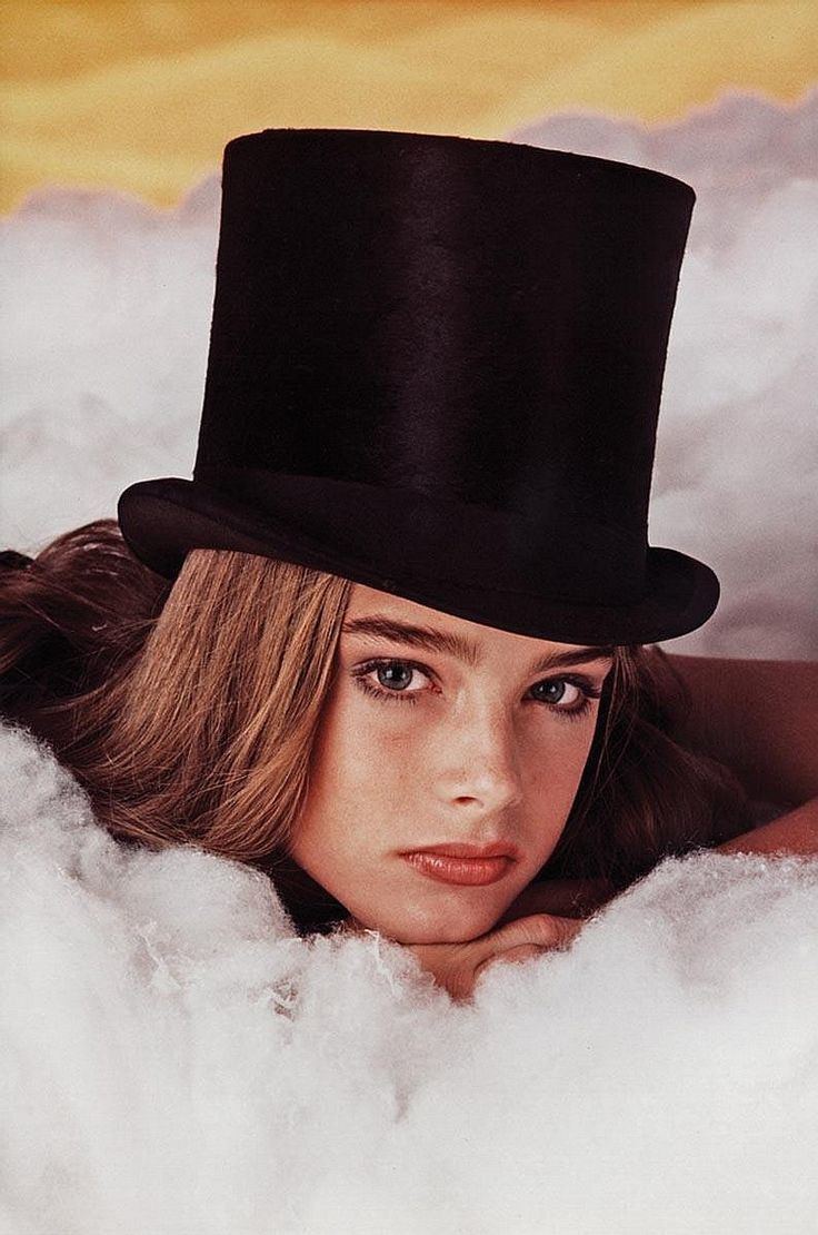 A picture of Brooke Shields Joven, photographed by Garry Gross. Brooke with a fierce look, a hair down, lying in a bed with a wool-like fabric, and wearing a black Zatanna hat