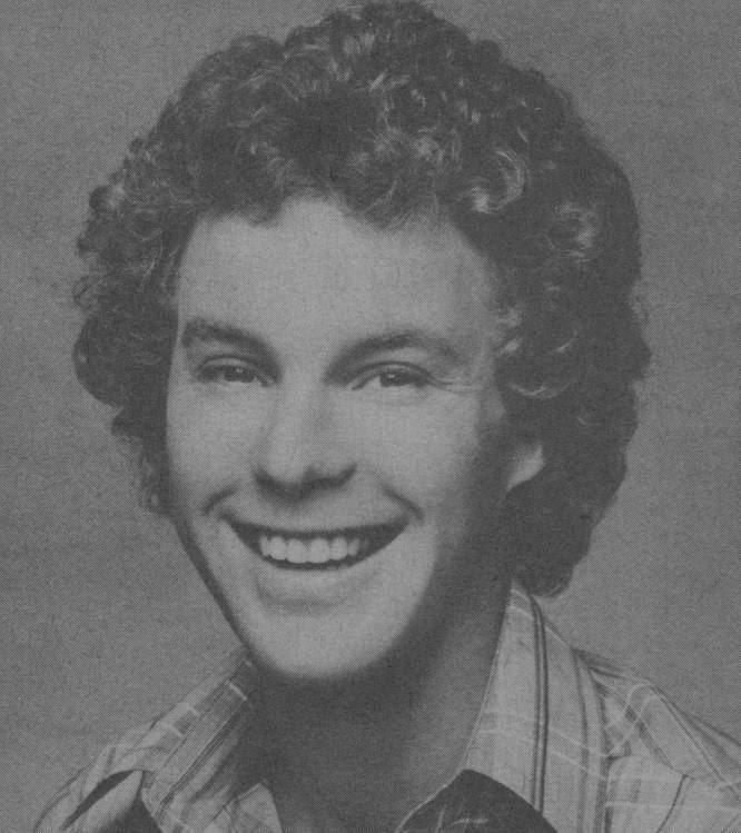 Gary Frank (actor) smiling, with curly hair and wearing a checkered polo shirt.