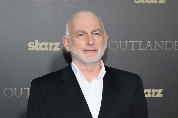 Gary Lewis smiling while wearing a black coat and white long sleeves