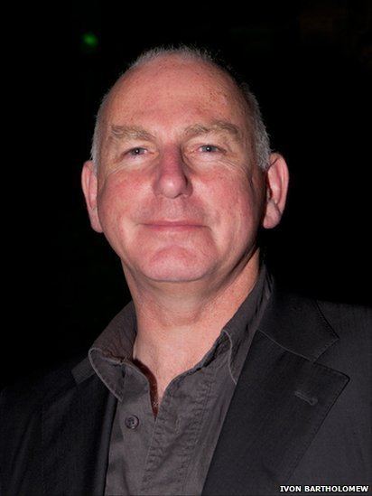 Gary Lewis smiling while wearing a black coat and brown long sleeves