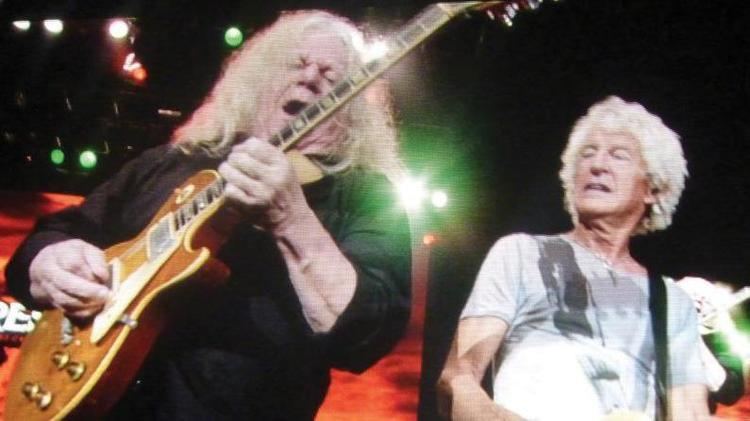 Gary Richrath and Kevin Cronin performing on stage, both have white hairs. Gary wearing black long sleeves while Kevin wearing a gray and white shirt.