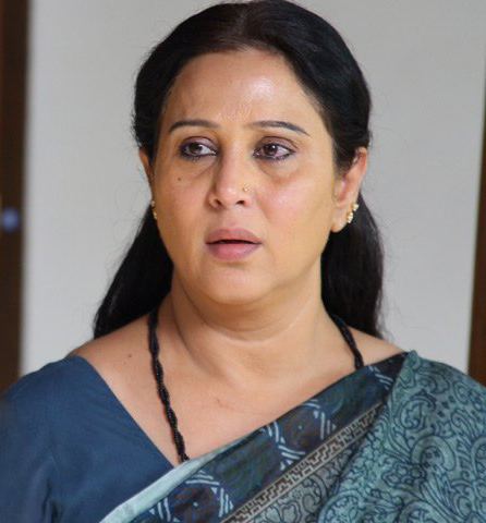 Geetha looking serious and wearing a blue saree and black beaded necklace