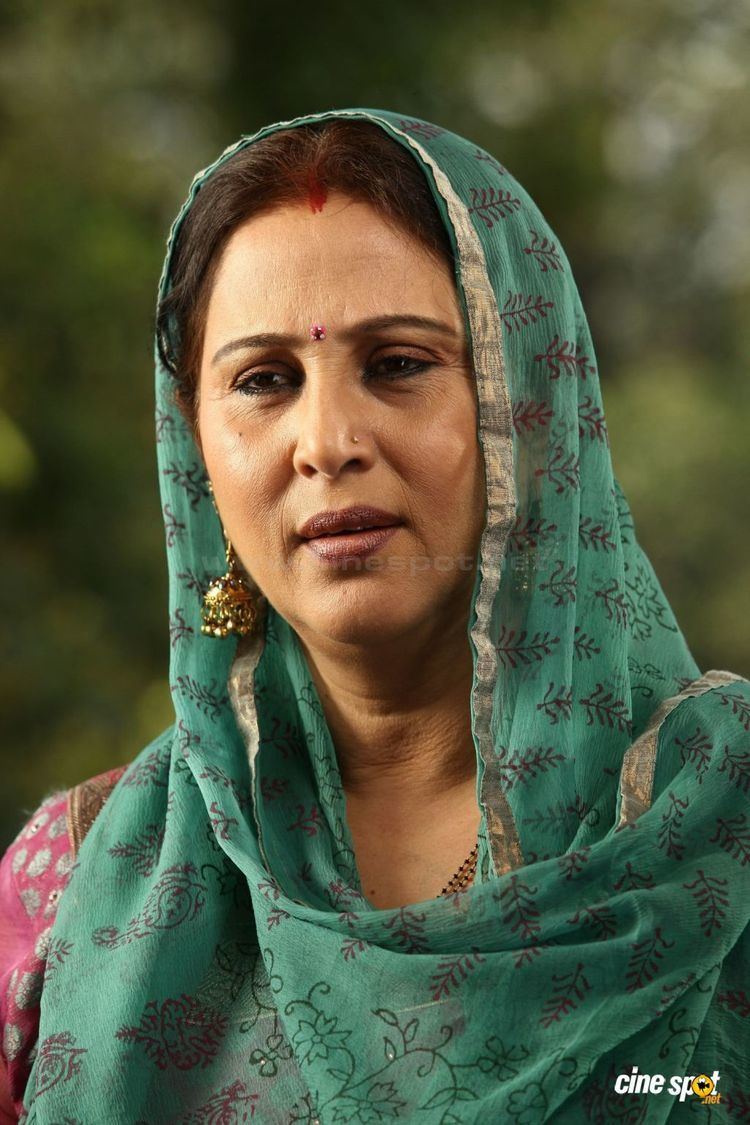 Geetha smiling and wearing a pink dress, dangling earrings and green shawl covering her head