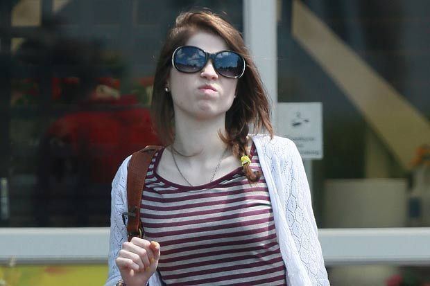 Gemma Barker walking and wearing a white long-sleeve over a red striped shirt as well as sunglasses while carrying a bag.