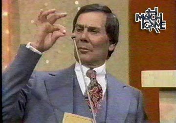 Gene Rayburn holding the microphone while hosting the Match Game and wearing white long sleeves, necktie, gray vest, and coat