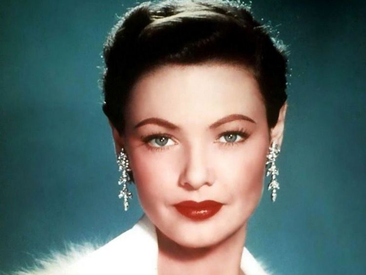 Gene Tierney with a fierce look, black hair, wearing earrings, and a white fur top.