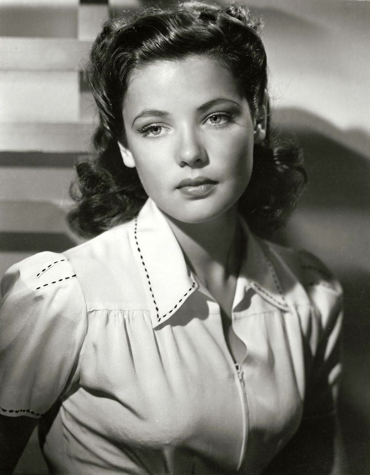 Gene Tierney with a serious face, short wavy hair, and wearing a white blouse with black lines.