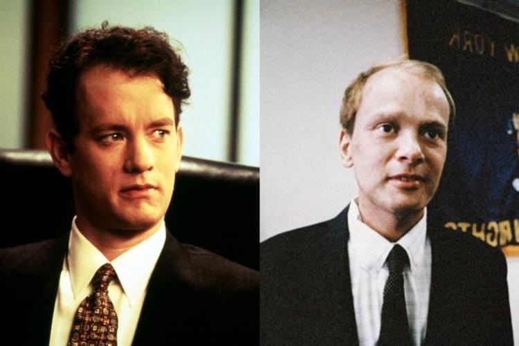On the left, Tom Hanks while looking afar. On the right, Geoffrey Bowers wearing a black coat, white long sleeves, and a black necktie
