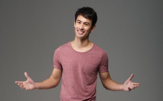 George Young smiling while his arms open and wearing a pink t-shirt