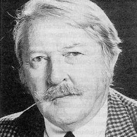 Georges Pichard looking serious with a mustache and wearing a white shirt with a black necktie under a plaid coat