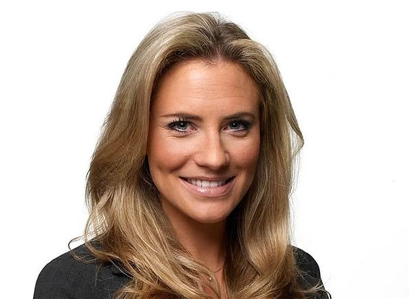 Georgie Thompson smiling, with wavy blonde hair, wearing a necklace, and a black blazer.