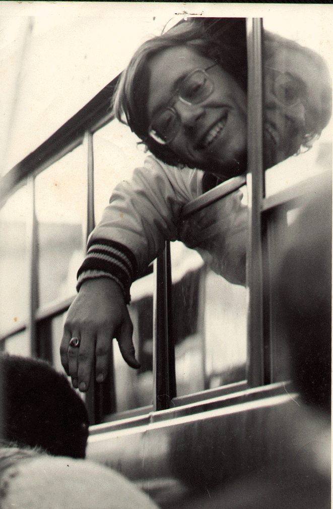 Gerry Bertier smiling, wearing eyeglasses with a ring on his finger while riding a bus.