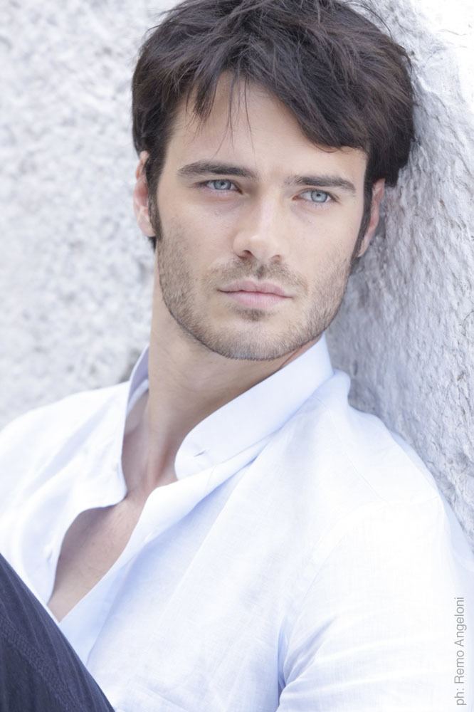 Giulio Berruti looking afar with a serious face, blue eyes, mustache, and beard while wearing a white long sleeve and black pants