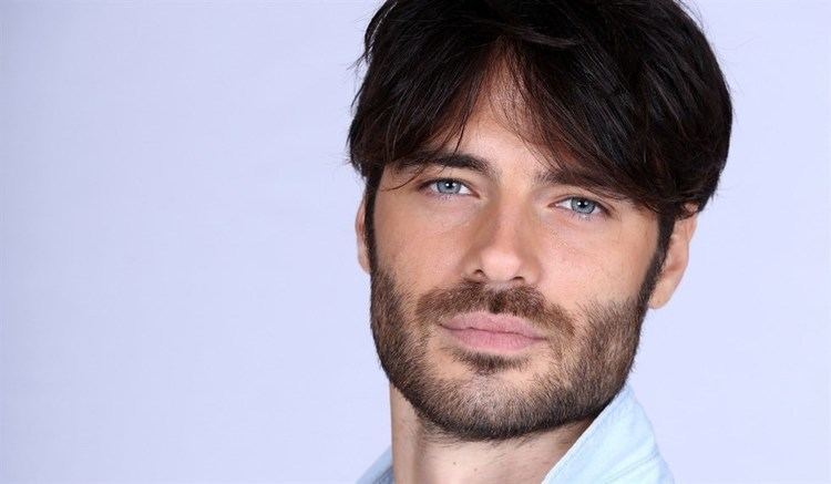 Giulio Berruti with a tight-lipped smile, blue eyes, mustache, and beard while wearing a white shirt