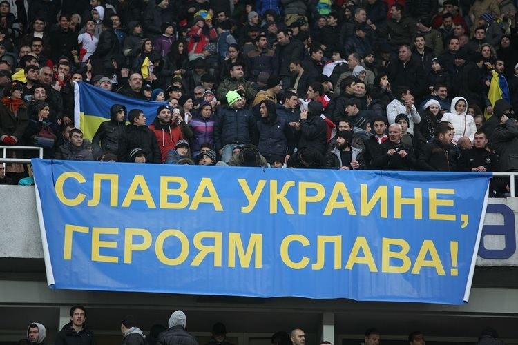 Ukrainian people at the stadium with a banner saying, "Glory to Ukraine, glory to heroes!”