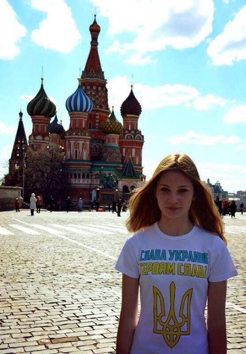 A girl posing in front of the Saint Basil's Cathedral, Moscow, Russia while wearing a white t-shirt printed with the slogan "Glory to Ukraine Glory to Heros" in the Russian language.