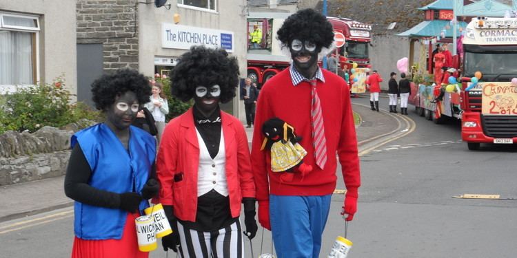 Three people dressed up as Golliwog dolls walking along the street.