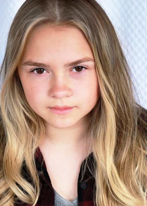 Gracie Prewitt with blonde curly hair while wearing a dark maroon blouse and gray inner blouse