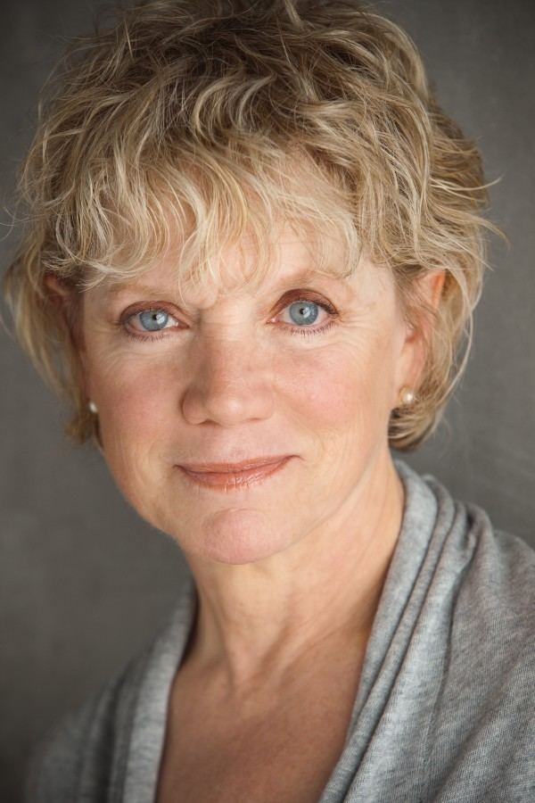 Gretchen Corbett smiles in gray background wearing a sleeve