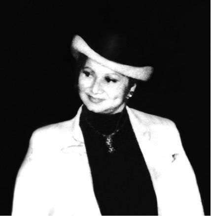 Griselda Blanco smiling while wearing a hat, blazer, turtle-neck blouse, and necklace