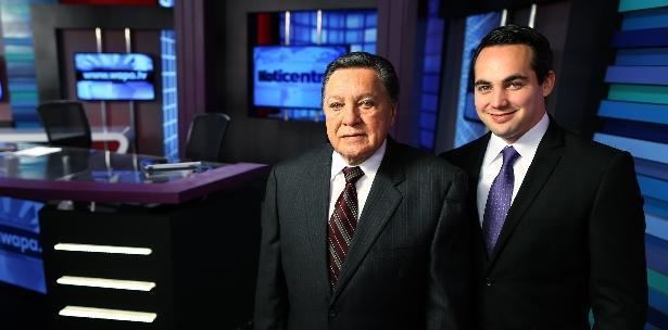 Guillermo José Torres inside the newsroom, wearing a black suit, white long sleeves, and striped tie, beside him is his son Guillermo José Torres, Jr. smiling, wearing a black suit, white long sleeves, and a purple tie.