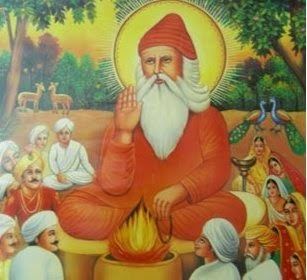 A colored painting, has a land trees and bushes at the back with two deer's at the left and two peacock at the right in the middle is a man sitting with a fire in front and surrounded by people wearing white Indian cap and white robes, in the middle, Guru Jambheshwaris serious, with his right hand open with his palm showing, left hand down holding a black lace,, looking up to his right with a yellow sun circle around his head, has white long hair beard and mustache, wearing a red-orange cap and a red-orange robe,