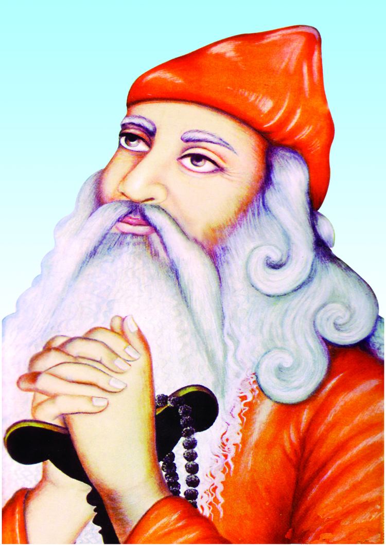 A colored painting, in a sky-blue background, Guru Jambheshwar is serious, praying with both hands holding a cane with a black bead necklace, looking up to his right, has white long hair beard and mustache, wearing a red-orange cap and a red-orange robe.