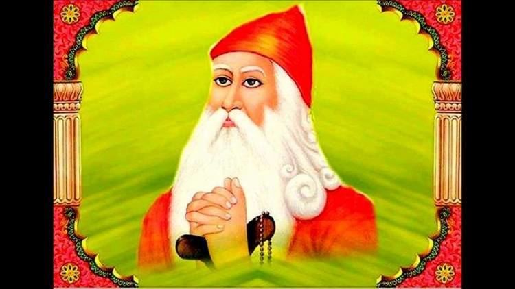 A colored painting, has red-orange border with yellow flowers and pillars on the corners, has yellow green background, Guru Jambheshwar is serious, praying with both hands holding a cane with a black bead necklace, looking up to his right, has white long hair beard and mustache, wearing a red-orange cap and a red-orange robe.