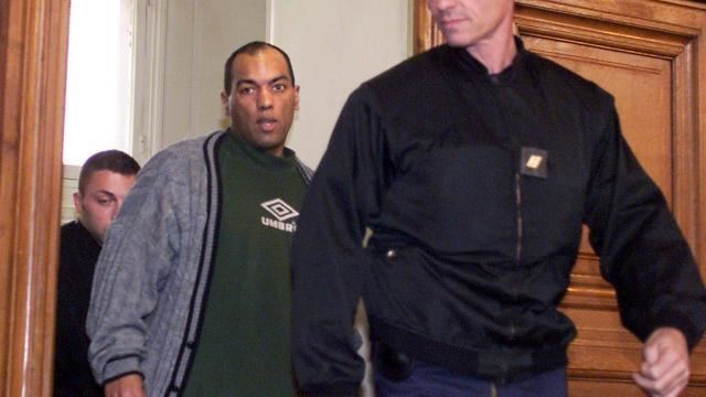 The arrival of Guy Georges at the trial court while wearing a black and gray knitted jacket and green t-shirt
