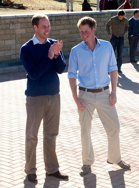 Prince William talking to Prince Harry while he is wearing a blue sweatshirt and brown pants