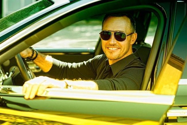 Gyorgy Gattyan smiling inside a car, wearing sunglasses, and black long sleeves.
