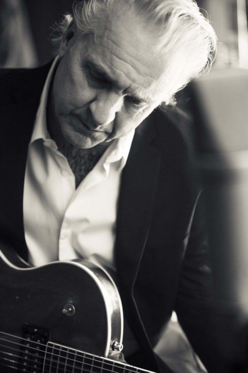 Neil Giraldo playing his guitar and wearing a white shirt under a black suit
