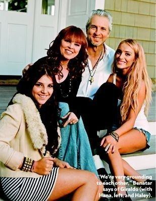 Haley Giraldo smiling with her blonde hair down and sitting beside her dad with her mom and sister Hana while wearing a white top and shorts