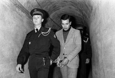 Hamida Djandoubi is accompanied by a French police officer to his execution while he is wearing a coat, inner shirt, and pants