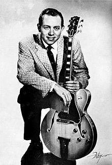 Hank Garland posing with a guitar and wearing a checkered suit and tie.