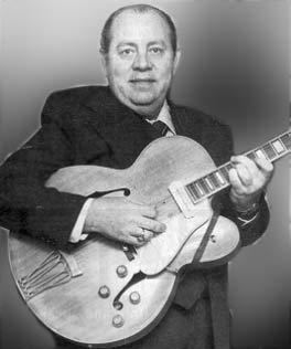 An older Hank Garland posing while holding a guitar and wearing a suit and tie.