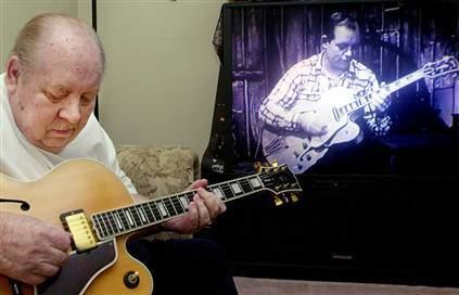 Hank Garland playing a guitar along a video of himself.