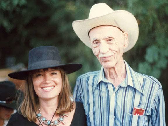 Hank Worden smiling while wearing a hat, and blue striped long sleeves, and the woman beside him smiling & wearing a black hat and black blouse