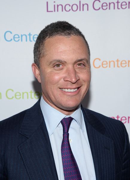 Harold Ford, Jr. smiling and wearing a suit, long sleeves, and a purple tie.