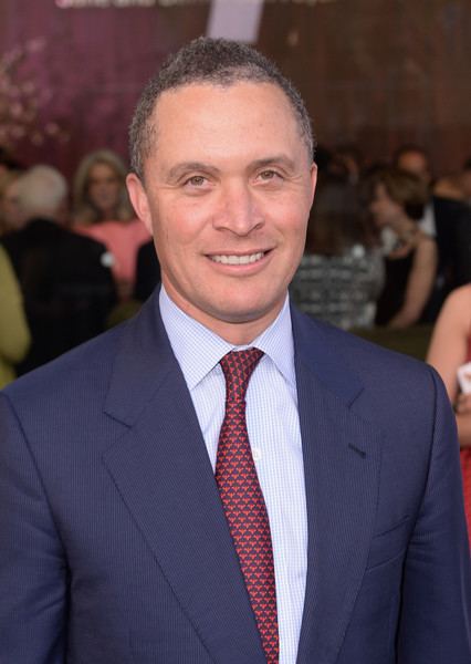 Harold Ford, Jr. smiling and wearing a blue suit, long sleeves, and a red tie.